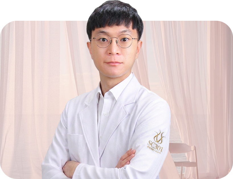 Professional portrait of a doctor in a white coat with glasses, arms crossed, in a soft-lit room.